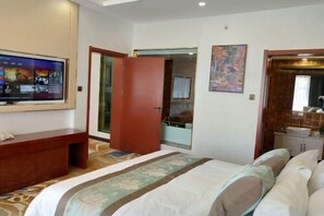 A hotel room with a bed, a TV mounted on the wall, a wooden desk, and a bathroom visible through an open door. - Yunshan Hotel (Jishishan)