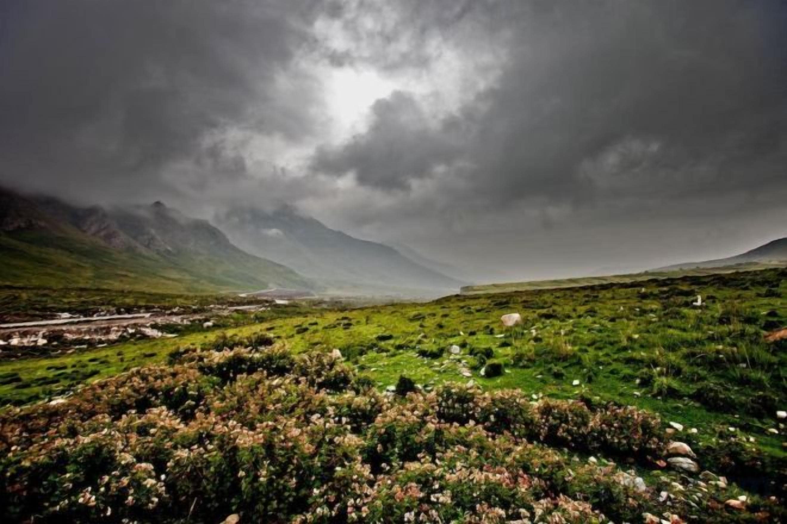 A landscape with a valley, mountains, and a cloudy sky.