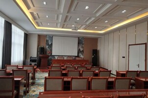 Un salón de conferencias con filas de mesas y sillas, una pantalla de proyector y un sistema de sonido.