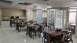 A dining area with multiple wooden tables and chairs, a kitchen area with appliances, and decorative white panels. - Yunshan Hotel (Jishishan)