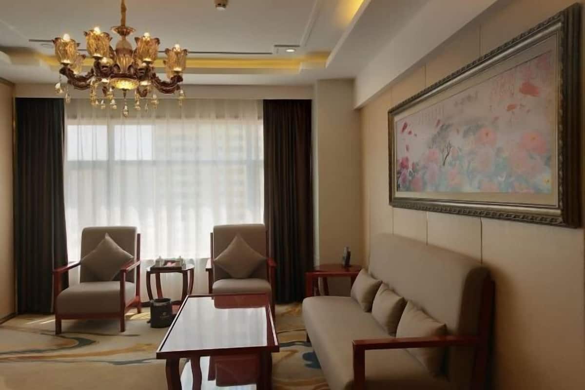 Habitación de hotel con candelabro, dos sillones, un sofá, una mesa de centro y un cuadro grande con motivos florales en la pared.