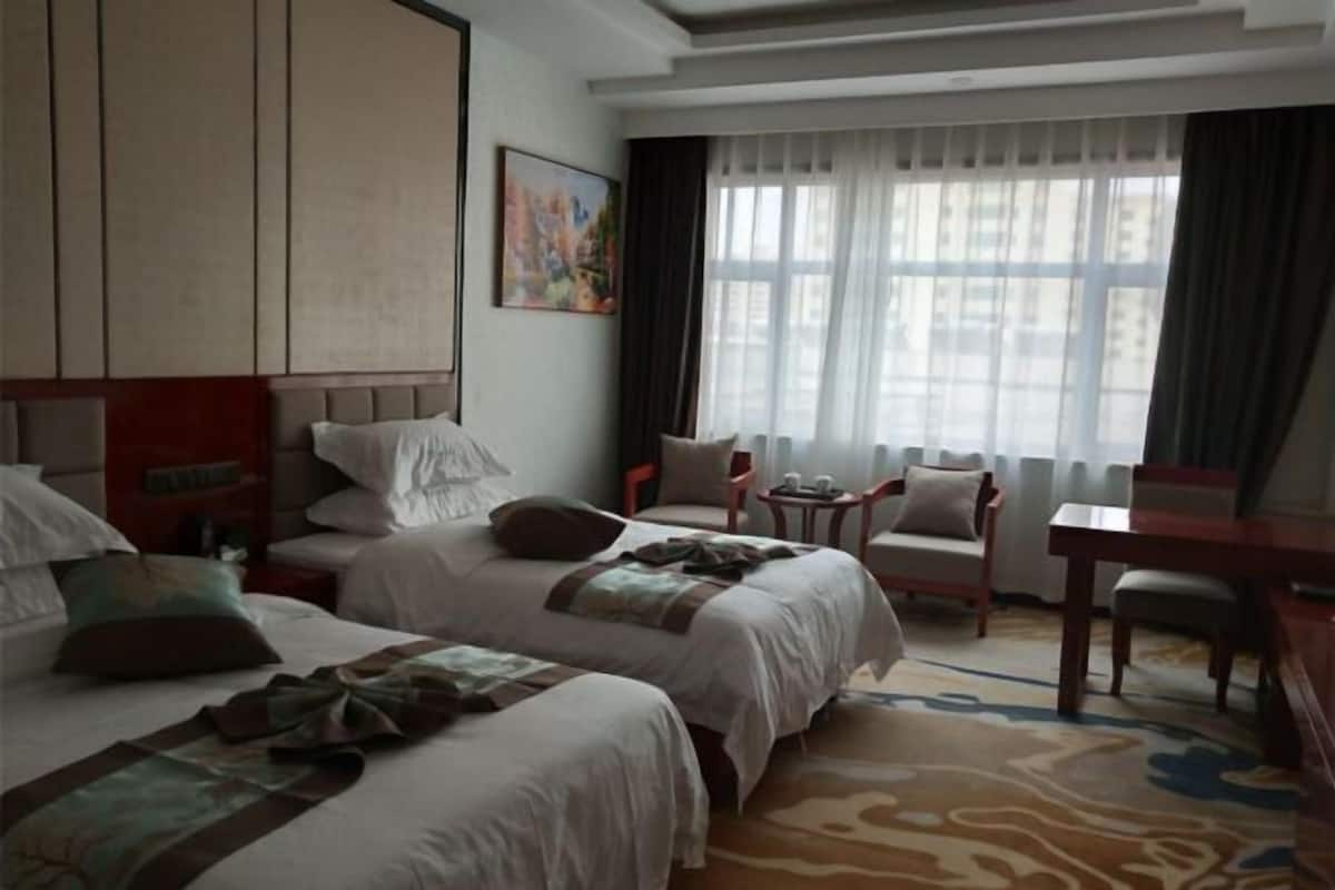 Una habitación de hotel con dos camas, un escritorio, una silla y una ventana con cortinas.