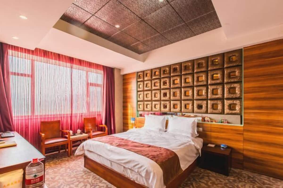 Habitación de hotel con cama, escritorio, silla, ventana con cortinas y pared con diseño decorativo.