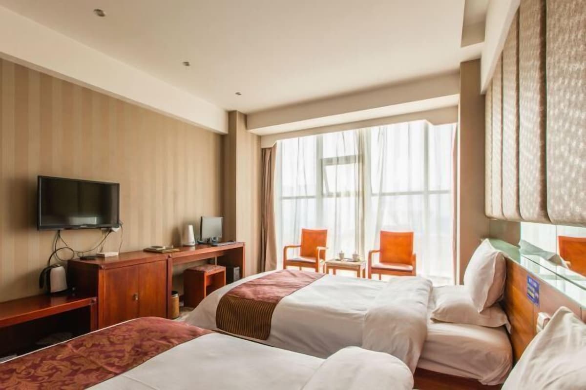 A hotel room with two beds, a desk with a computer, a television, and a large window with curtains.
