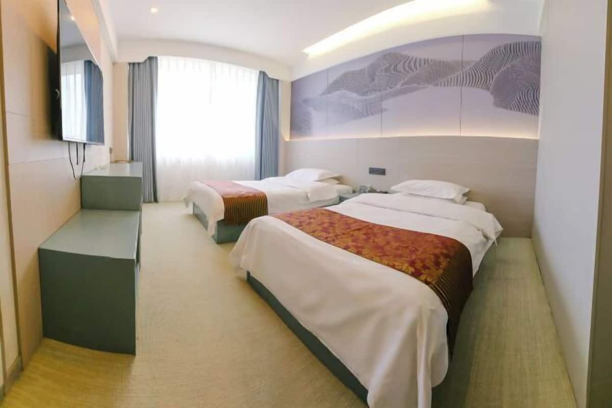 Habitación de hotel con dos camas, un escritorio, un espejo grande y una obra de arte en la pared.