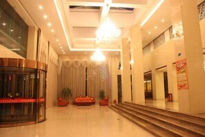 Un vestíbulo de hotel con una imponente escalera, un mostrador de recepción y un candelabro.