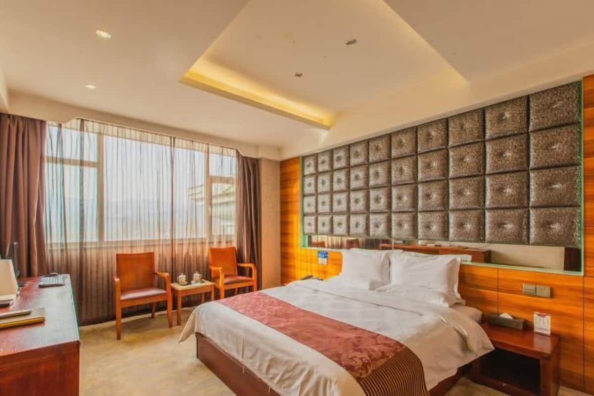 Una habitación de hotel con una cama grande, un escritorio con silla, una ventana con cortinas y un cabecero decorativo.