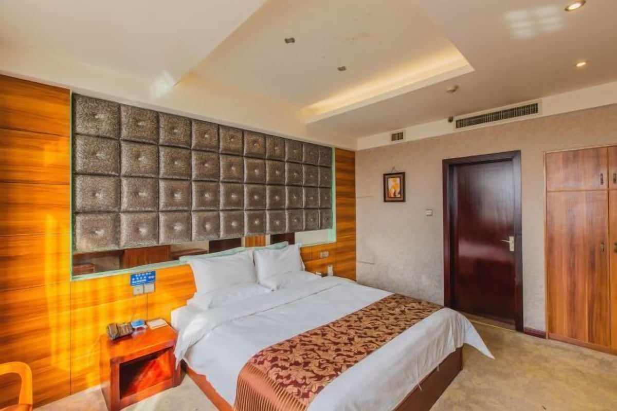 A hotel room with a large bed, a wooden headboard, a wooden wardrobe, and a small bedside table.