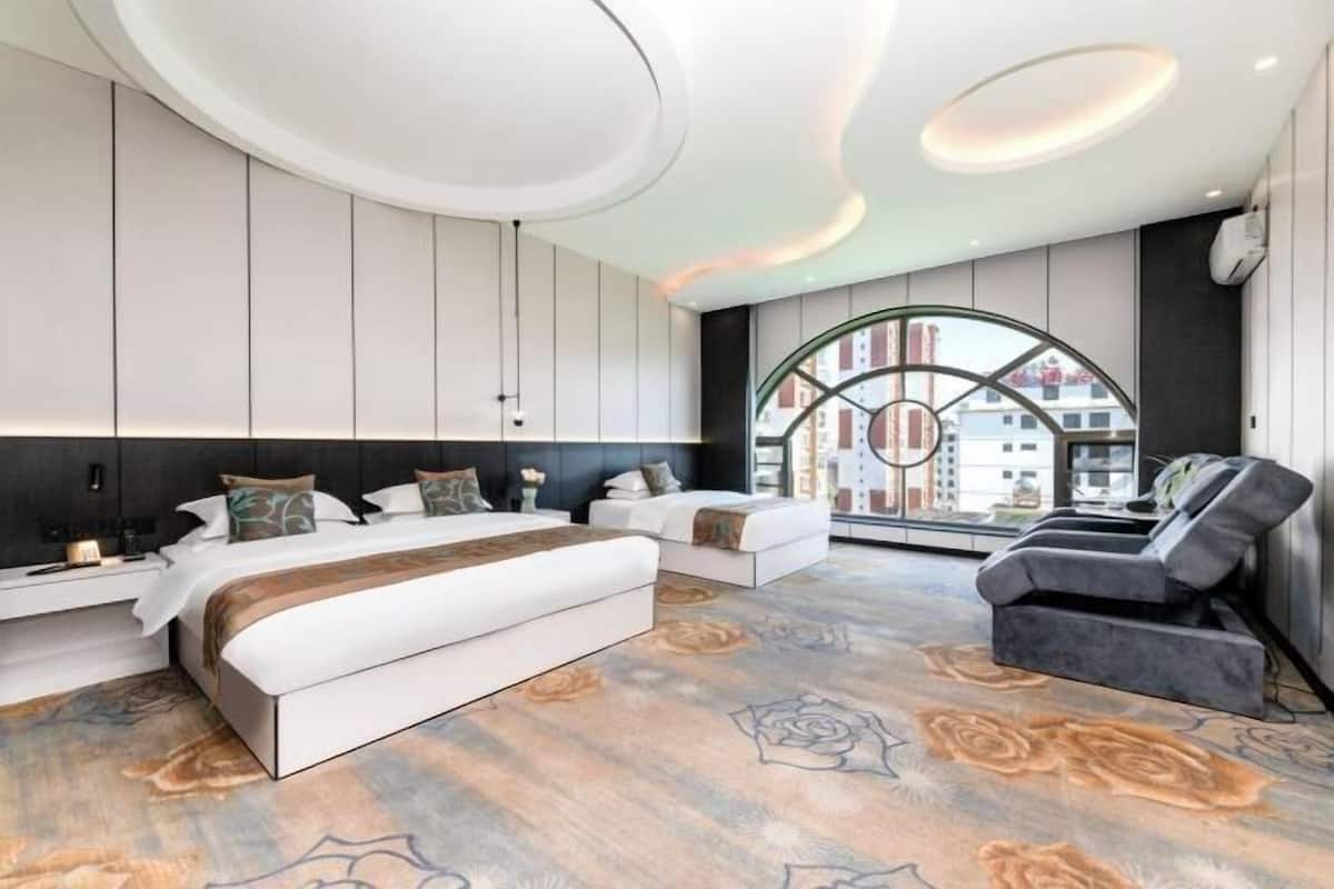 A modern hotel room with a large bed, a seating area, and a view of buildings through a circular window.