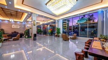 A modern hotel lobby with a chandelier, seating areas, and a reception desk.