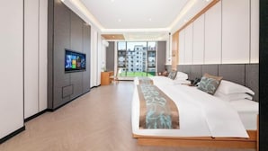 Une chambre d’hôtel moderne dotée d’un grand lit, d’un téléviseur fixé au mur et offrant une vue sur la ville grâce à de grandes fenêtres.