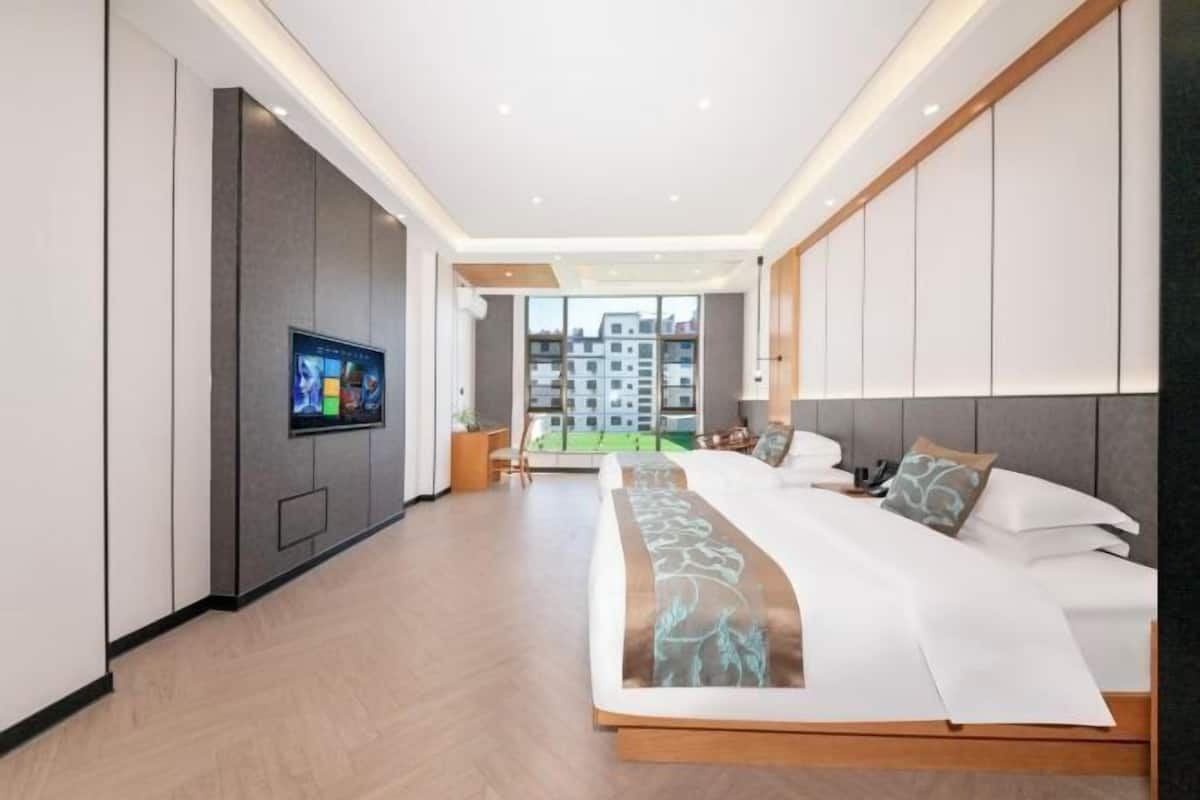 A modern hotel room with a large bed, a television mounted on the wall, and a view of the city through large windows.