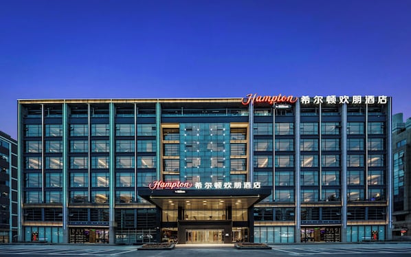 A modern hotel building with a prominent 'Champion' sign, large windows, and a well-lit entrance. - Hampton by Hilton, Yuhang High Speed Railway Station, Hangzhou (Jiaxing)