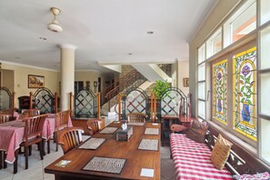 A dining area with a wooden table, chairs, and a bench. There is a staircase with a railing and a view of the outside through large windows. - Puri Sawo Manila (Jakarta)