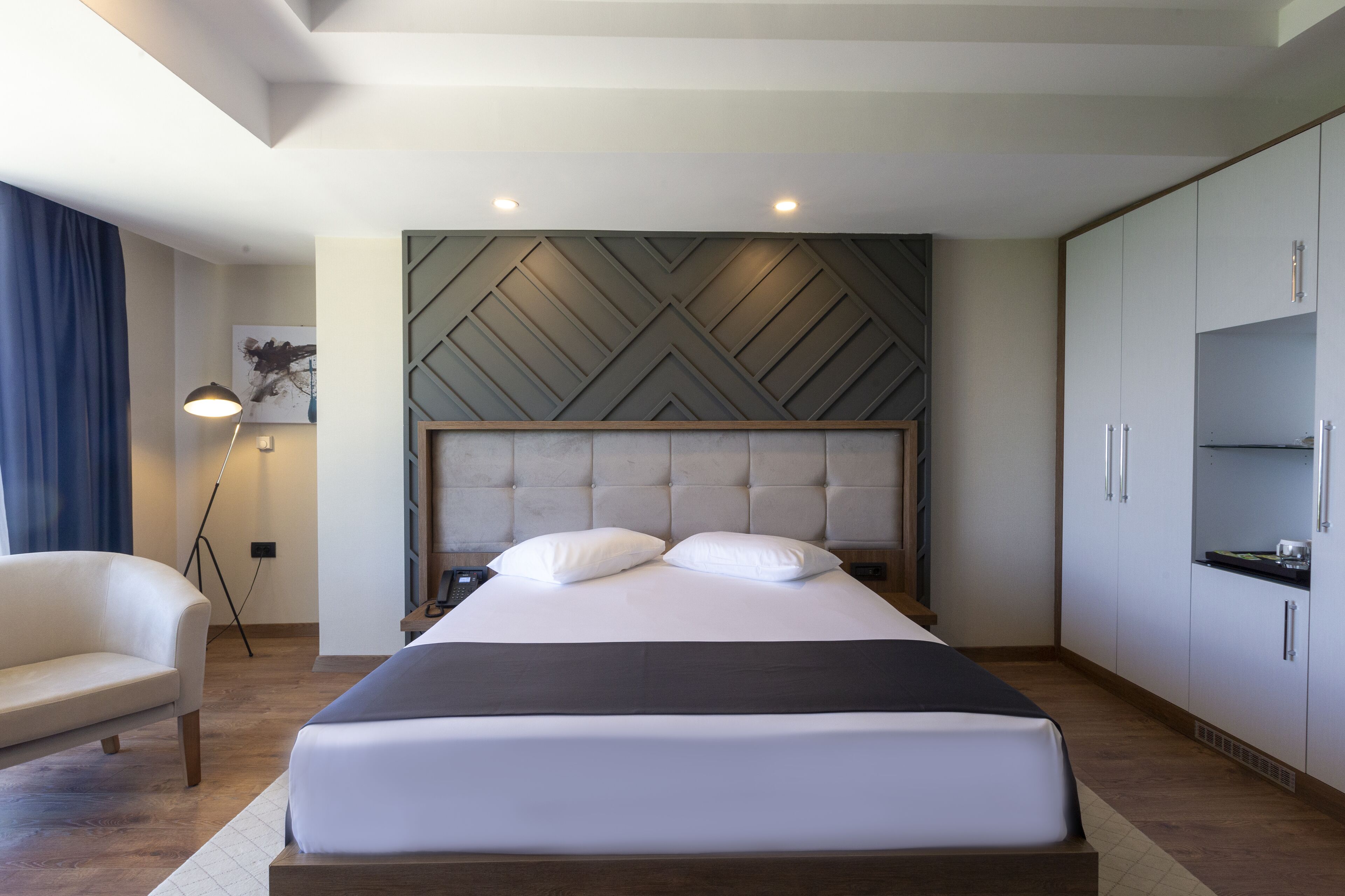 A modern hotel room with a large bed, a sofa, a wardrobe, and a floor lamp.