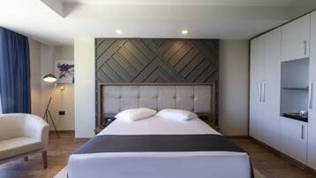 A modern hotel room with a large bed, a sofa, a wardrobe, and a floor lamp.