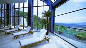 A sunlit room with large windows, wooden lounge chairs, and a potted plant. - Cabir Deluxe Hotel (Sapanca)