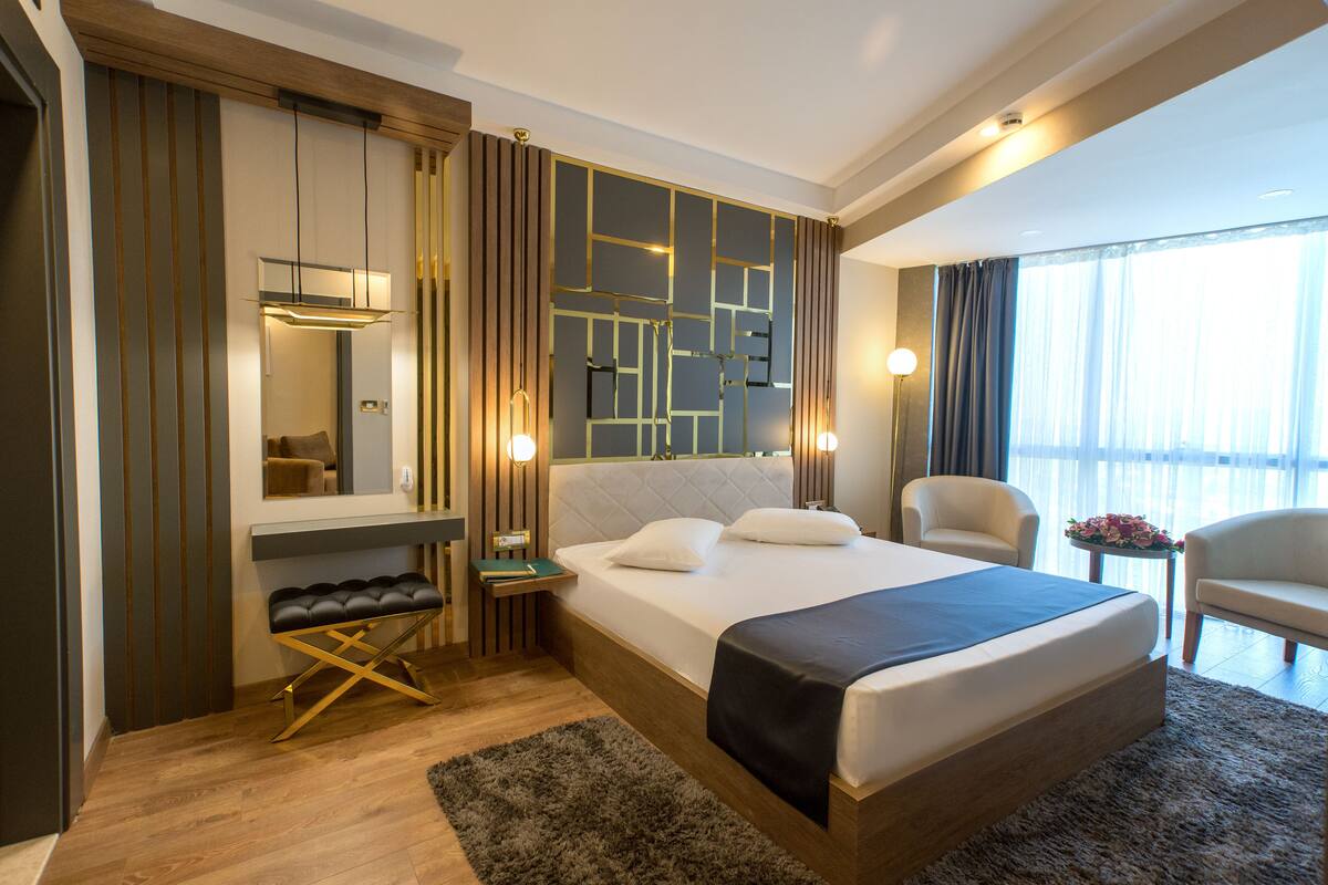 Una habitación de hotel moderna con una cama grande, un escritorio, una silla y vistas al exterior.