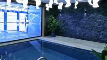 Ein Schwimmbecken mit klarem Wasser, eine Topfpflanze und moderne Deckenleuchten.