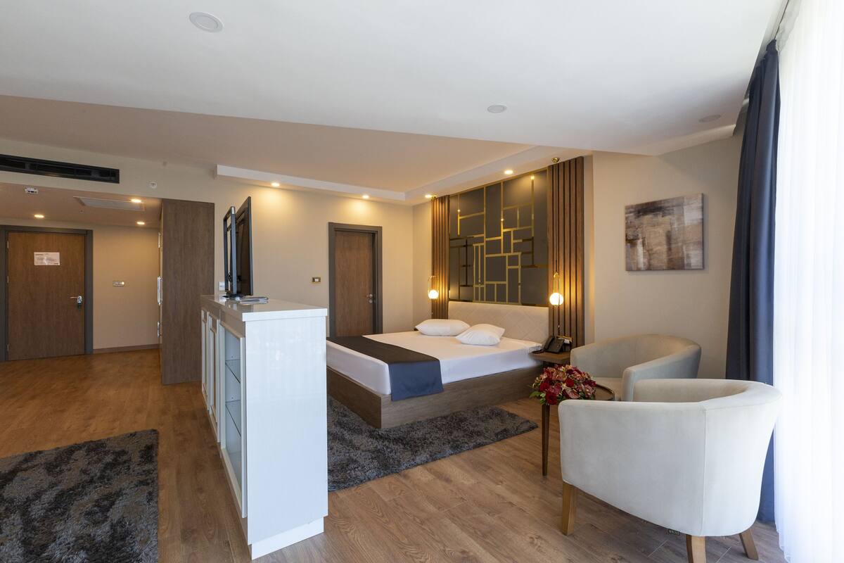Una habitación de hotel moderna con una cama, un escritorio, una silla y un ventanal grande.
