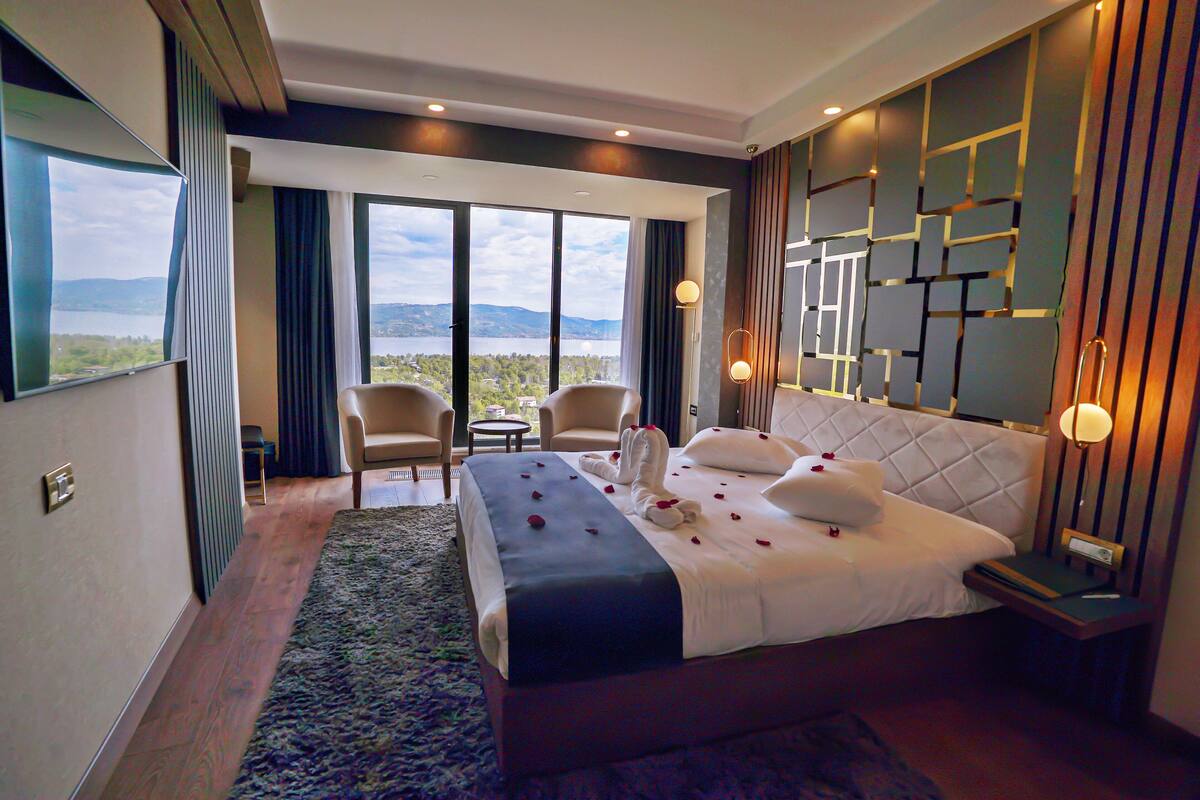 Habitación de hotel con una cama grande, dos sillones, vistas al exterior y un diseño moderno en la pared.