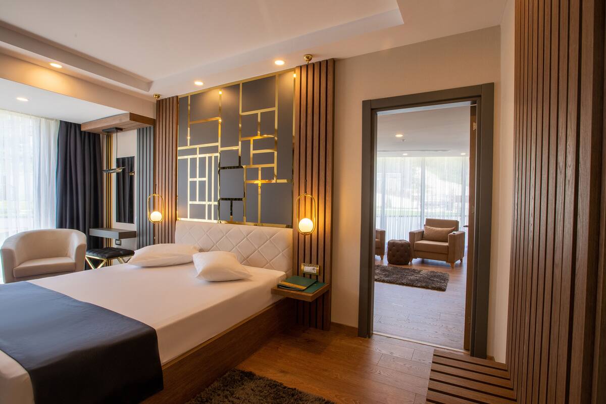 Una habitación de hotel moderna con una cama grande, mesitas de noche, un espejo y vistas al área de estar.