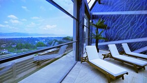 A balcony with a view of a cityscape and a body of water. There are three white lounge chairs and a small potted plant. - Cabir Deluxe Hotel (Sapanca)