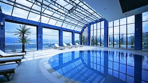 An indoor swimming pool with clear glass walls, lounge chairs, and a view of the outdoors. - Cabir Deluxe Hotel (Sapanca)