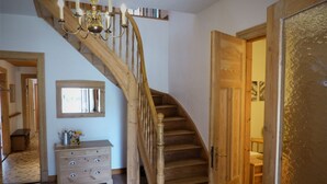 Un escalier en bois orné d’un lustre, un banc en bois, une commode et une porte.