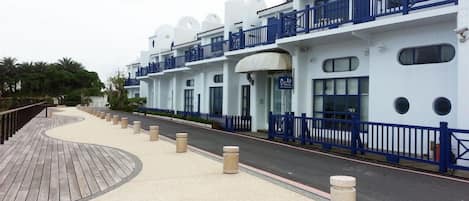A waterfront hotel with a curved wooden deck, a blue railing, and a white facade with balconies.