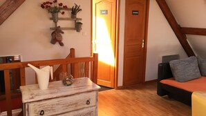 A cozy room with a wooden ceiling, a bed with a red and black bedspread, a white dresser with drawers, a wooden chair, and a shelf with plants and a teddy bear.