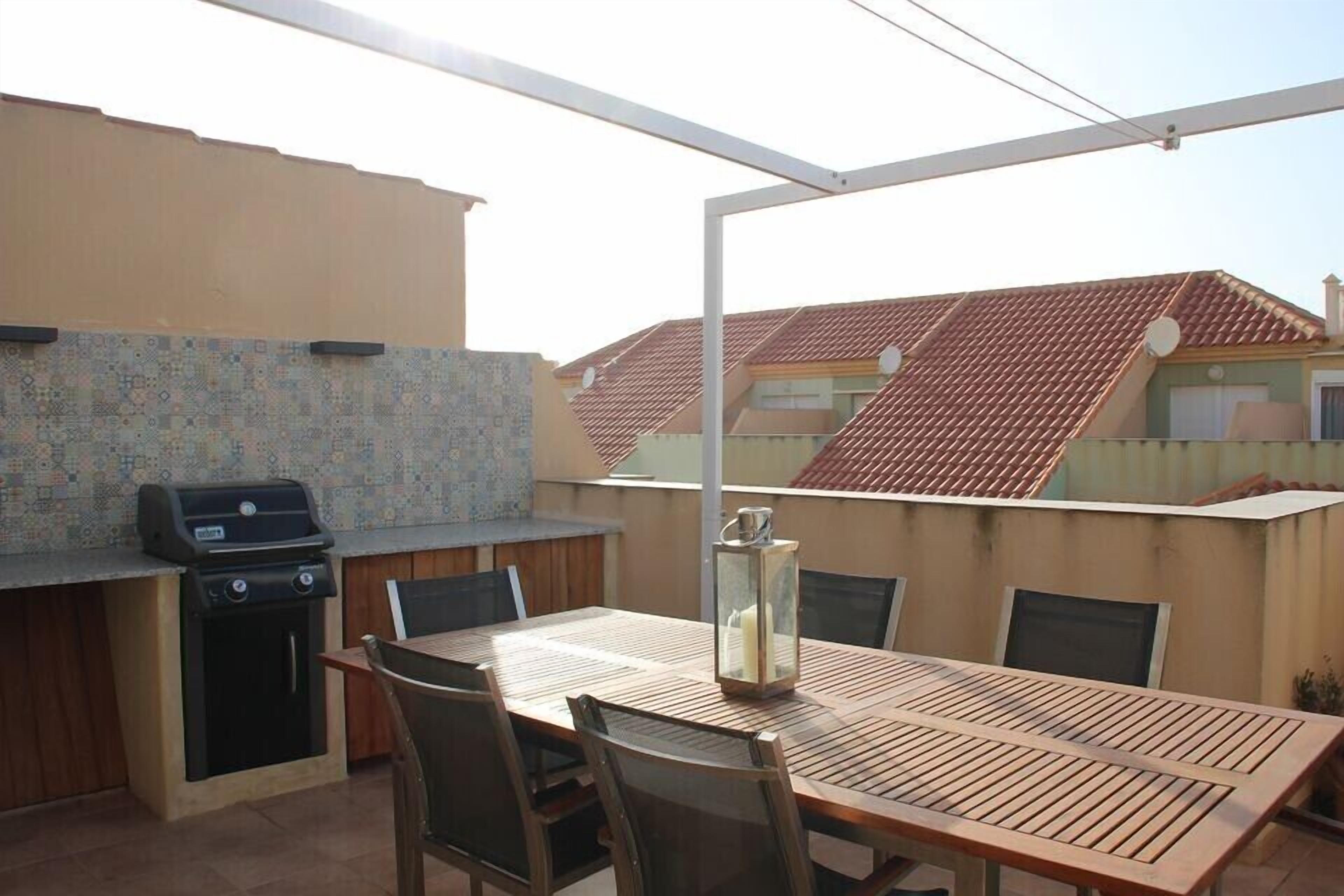 Une terrasse extérieure avec un barbecue, une table et des chaises.