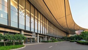 A modern hotel with a curved facade, large windows, and a well-maintained entrance area. - MeiChen Hotel( within the terminal building of Beijing Daxing International Airport) (Beijing)