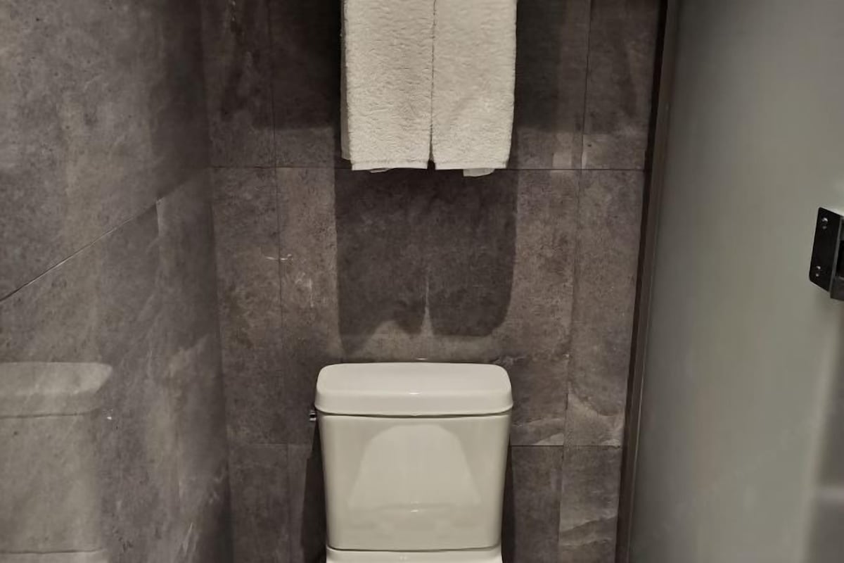 Une salle de bain avec des toilettes, une serviette accrochée au mur et un espace douche.