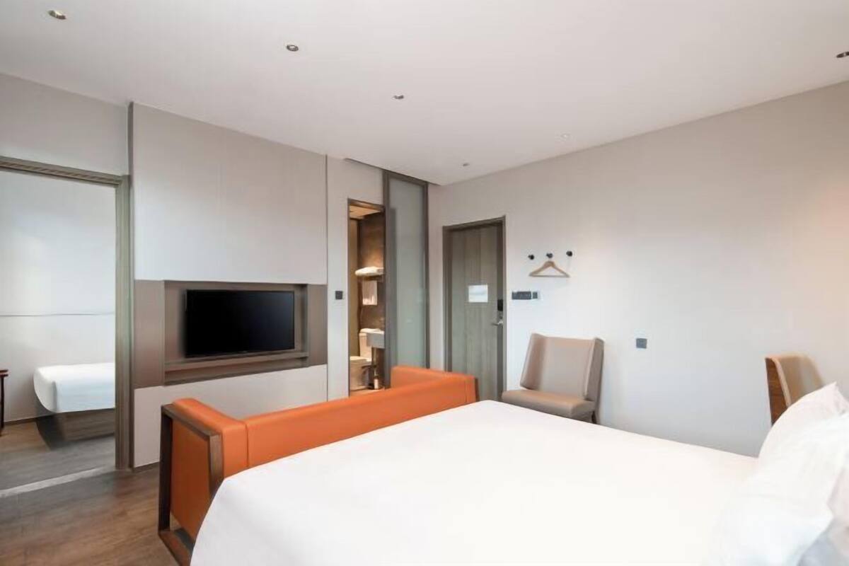A hotel room with a bed, a TV, a seating area with a chair, and a wardrobe.