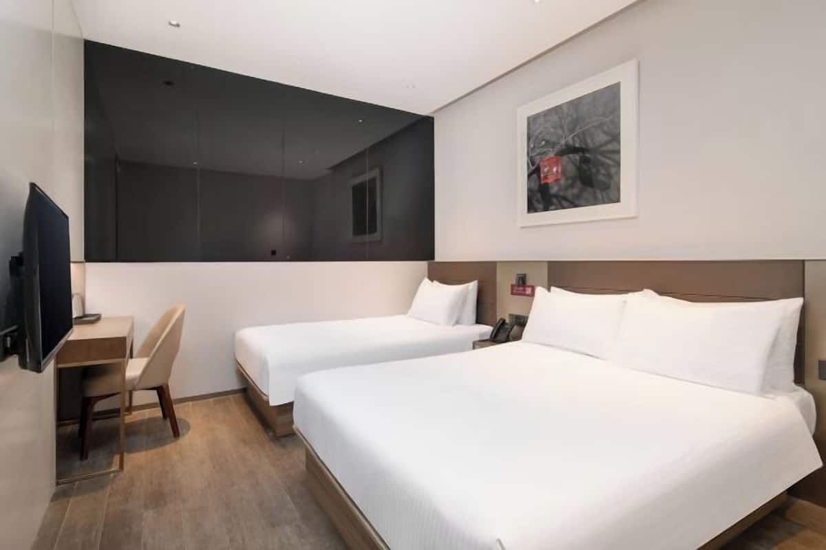 A hotel room with two beds, a desk, a chair, a TV, and a framed picture on the wall.