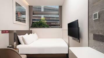 Una camera d'albergo moderna con un letto, una televisione, una finestra con vista e una piccola pianta.