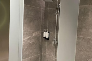 A shower area with a wall-mounted towel rack holding two bottles, a showerhead, and a handheld shower attachment. - MeiChen Hotel( within the terminal building of Beijing Daxing International Airport) (Beijing)