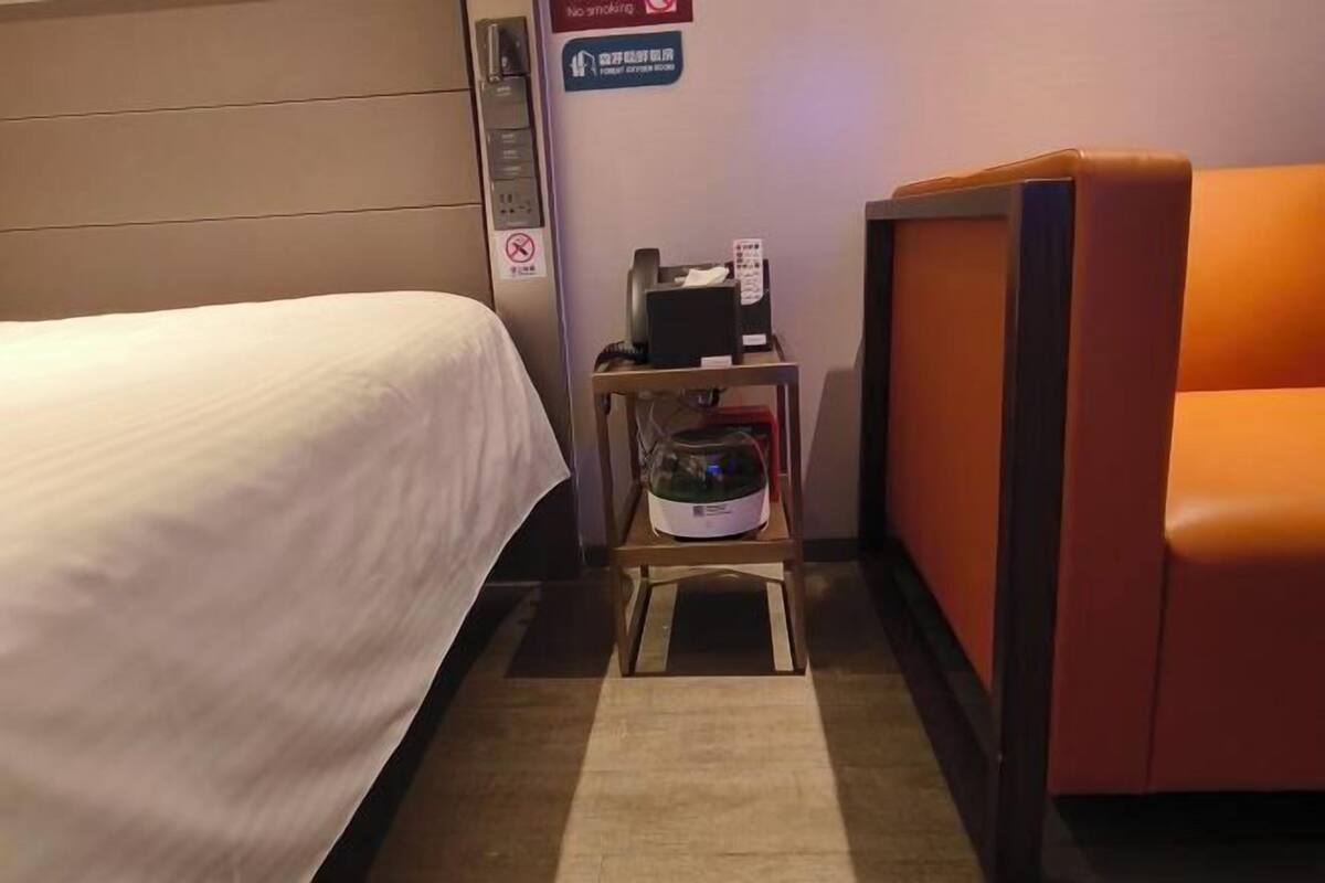 A hotel room with a bed, a small table with a microwave, a chair, and a sign indicating no smoking.