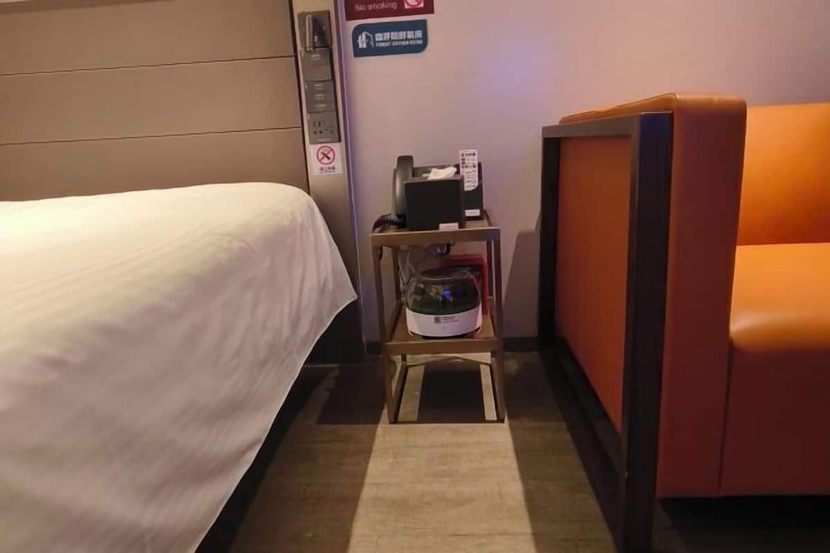 A hotel room with a bed, a small table with a microwave, a chair, and a sign indicating no smoking.
