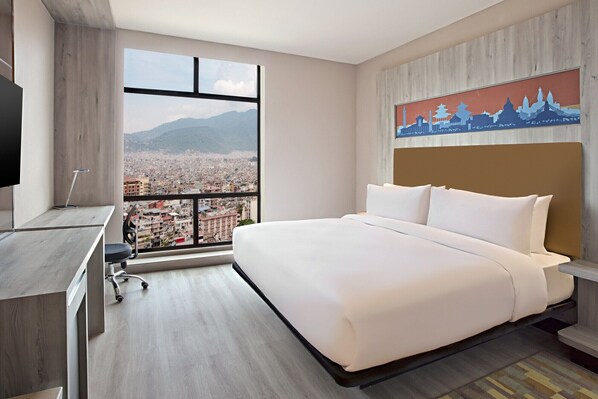 Une chambre d’hôtel avec un grand lit, un bureau avec une chaise, une télévision et une vue sur le paysage urbain par une grande fenêtre.