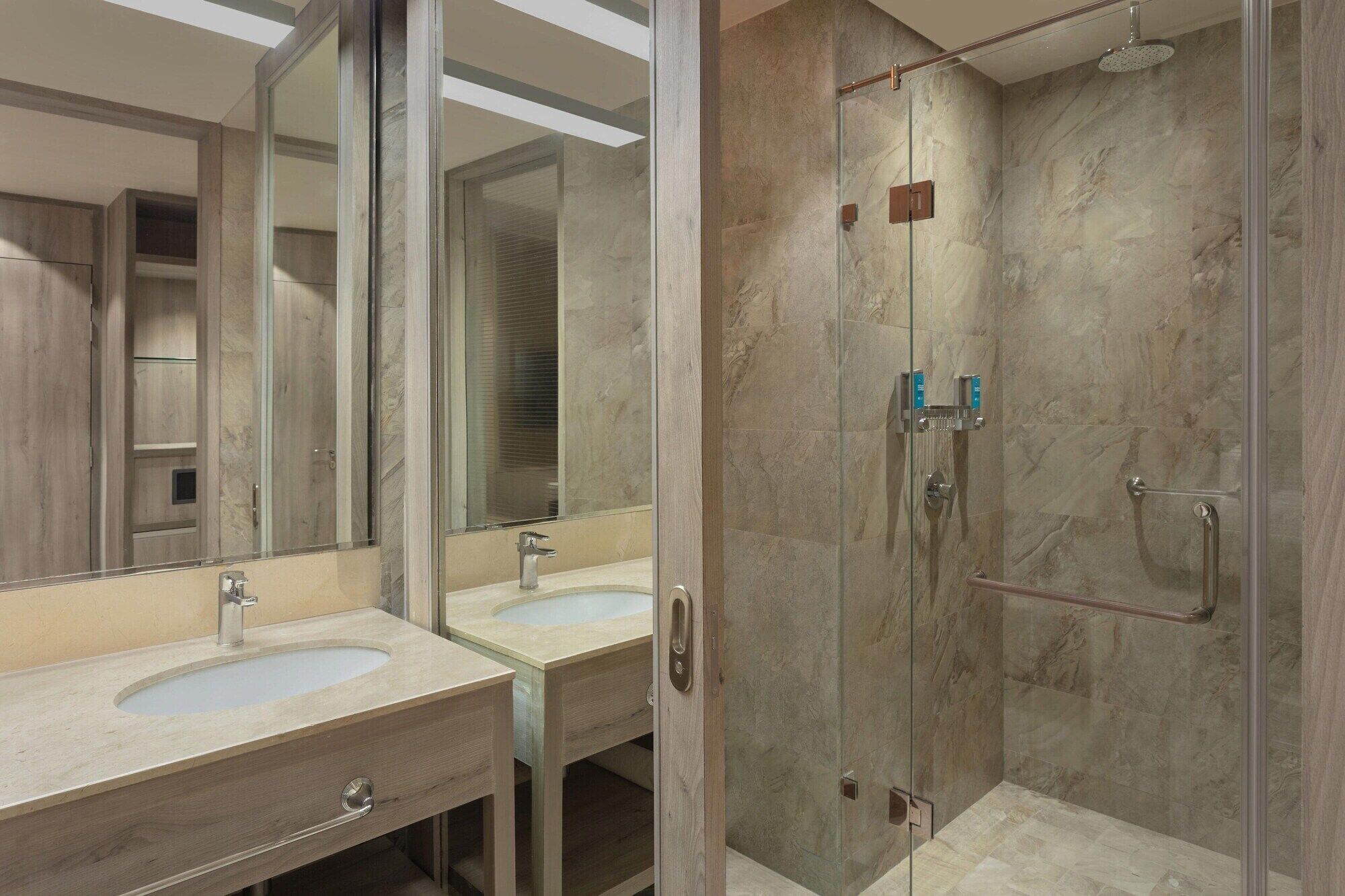 A modern bathroom with two sinks, a glass shower enclosure, and a large mirror.