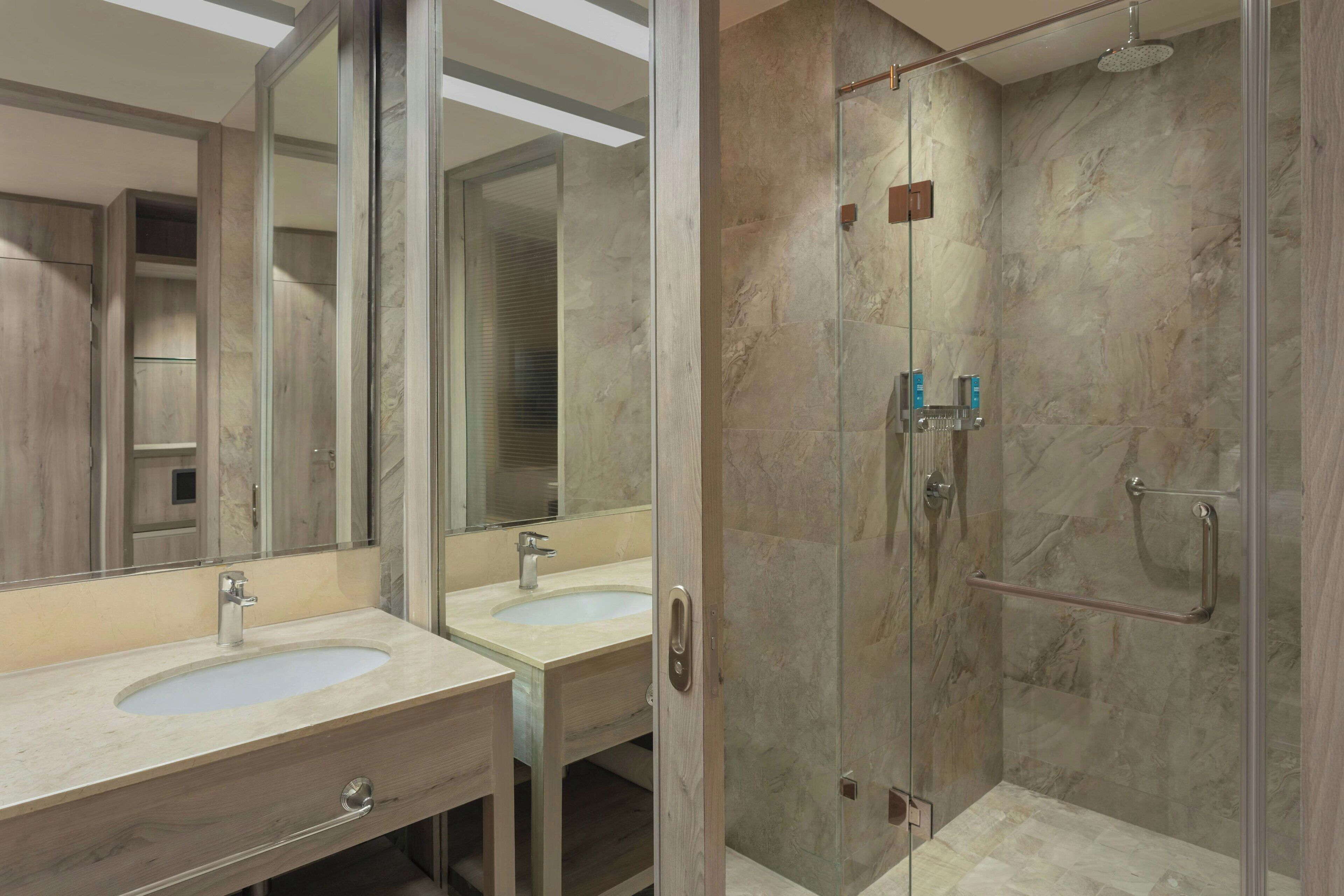 Une salle de bain moderne avec deux lavabos, une douche à l’italienne et un grand miroir.