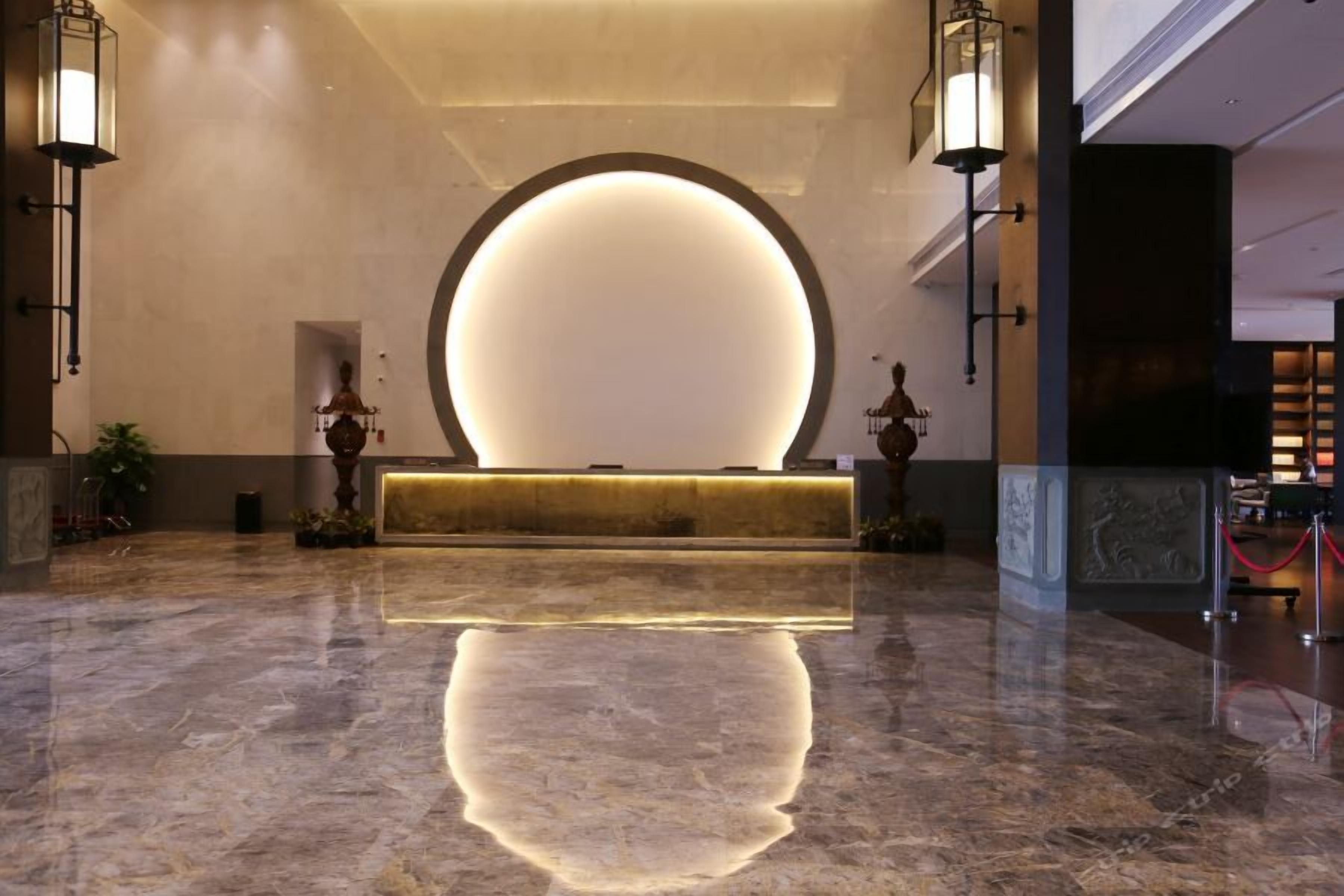 A lobby with a reception desk, marble flooring, and wall-mounted lighting fixtures.