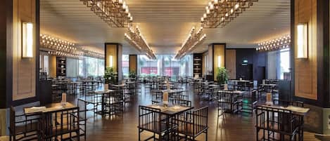 A spacious dining area with multiple tables and chairs, a modern ceiling design, and large windows allowing natural light.