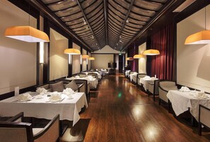 A restaurant with long tables, chairs, and overhead lighting. - Amitabha Hotel (Fuzhou)