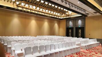 A conference room with rows of white chairs, a patterned carpet, and a ceiling with multiple light fixtures.