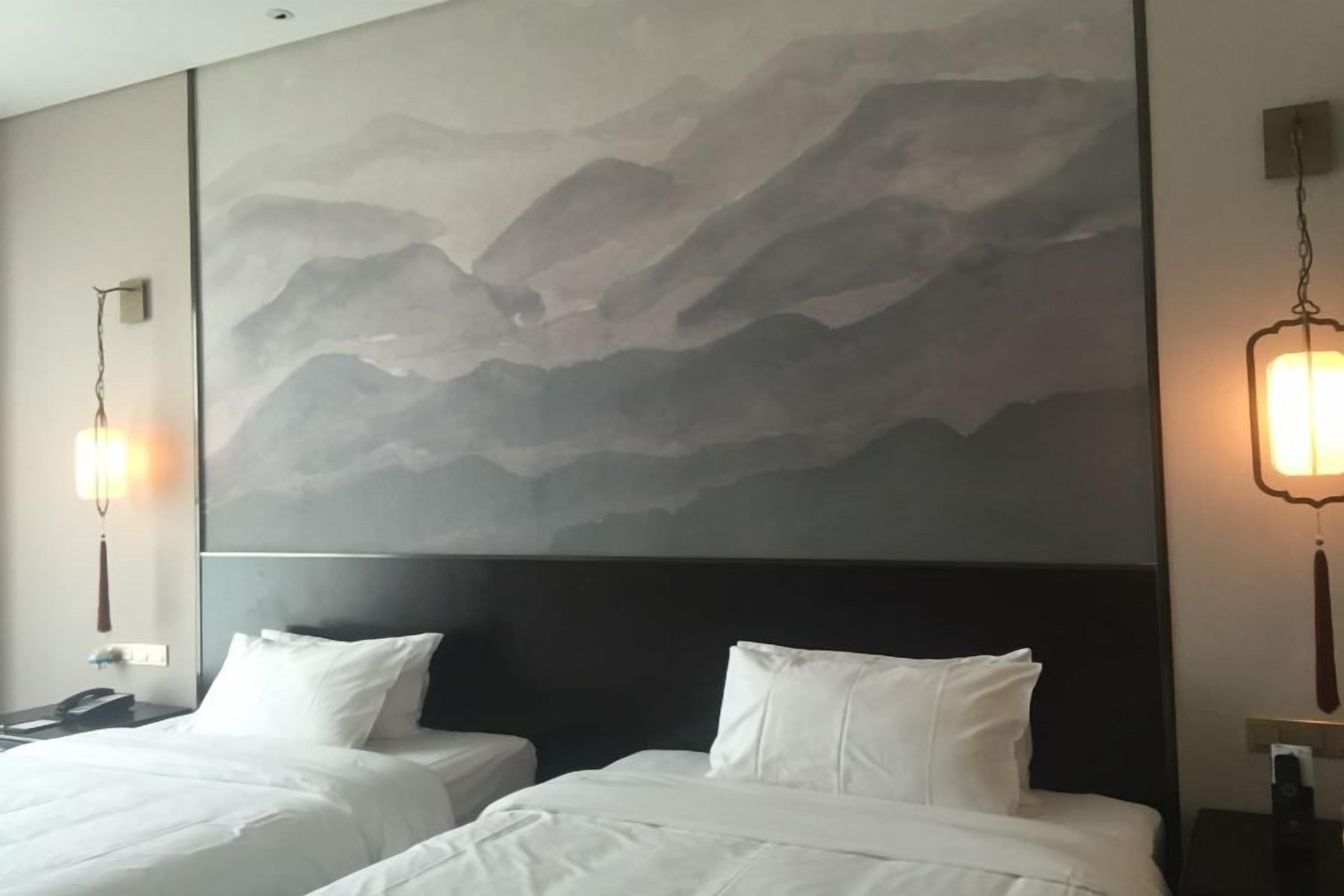 A hotel room with two beds, a large wall mural, and bedside lamps.