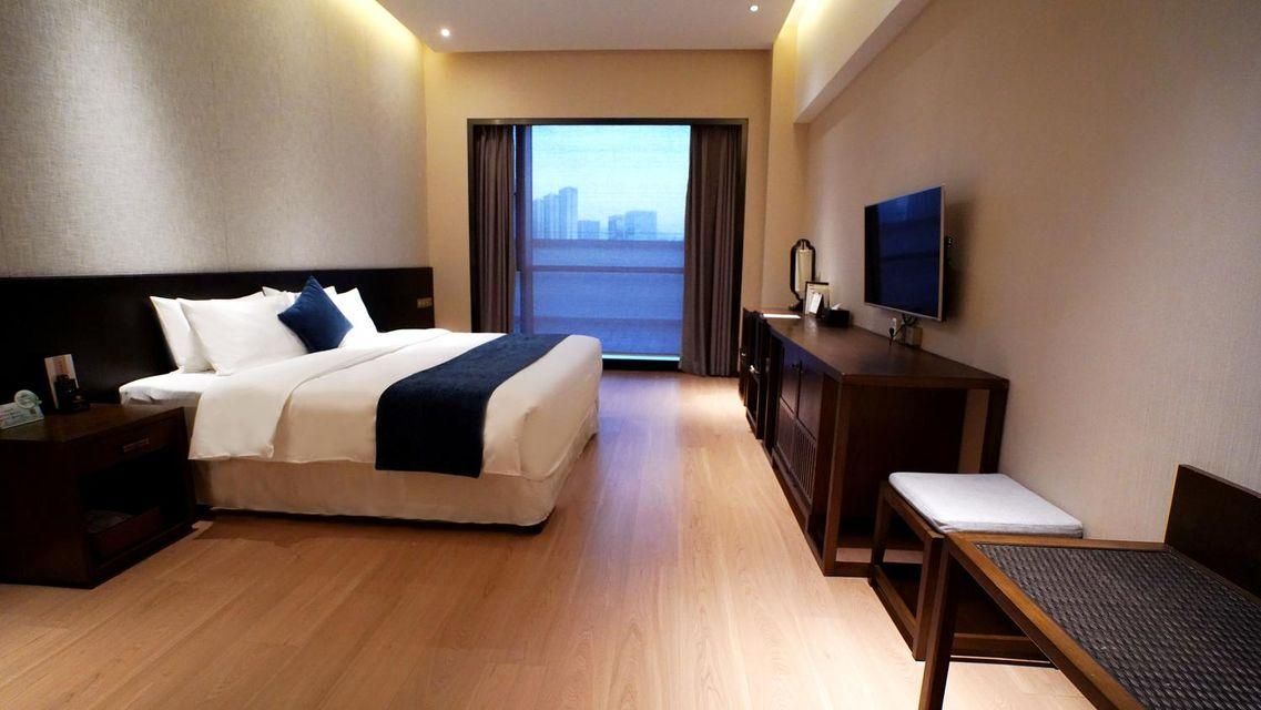 Habitación de hotel con cama, escritorio, televisor y vista a un paisaje urbano a través de un ventanal grande.