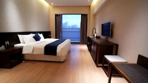 A hotel room with a bed, a desk, a television, and a view of a cityscape through a large window. - Amitabha Hotel (Fuzhou)
